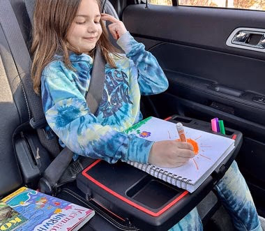 child drawing on car tray with books nearby