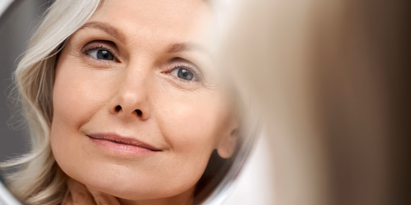 mature woman looking in mirror with glowing skin