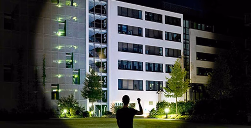 person holding flashlight illuminating a building at night