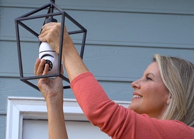 woman installing security camera into outdoor light fixture